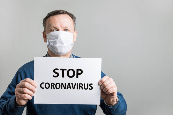 Adult man in protective medical mask holding white blank with text - Stop Coronavirus. Covid-19. Quarantine. Stay at home. - Fotoğraf, Görsel