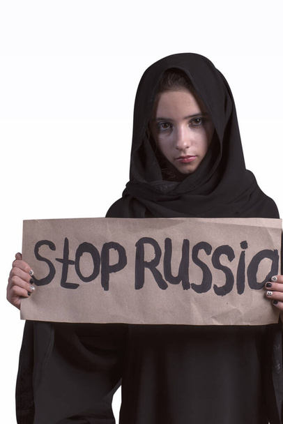 Traditional Arabic Muslim woman in stylish abaya.Arab young girl with a sad face dressed in black abaya with the text in her hands stop Russian. Russia aggressor in Syria. Muslim girl in black abaya. - Photo, Image