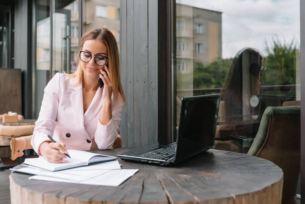 Portrait of smiling pretty young business woman in glasses sitting on workplace - Foto, Bild