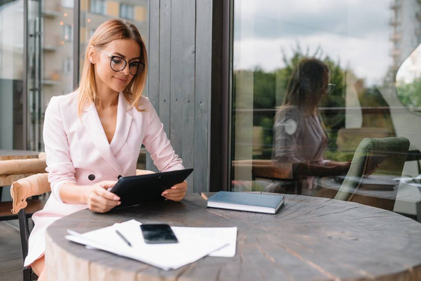 Portrait of young attractive businesswoman examining paperwork in bight light office interior sitting next to the window, business woman read some documents before meeting, filtered image - Foto, Imagem