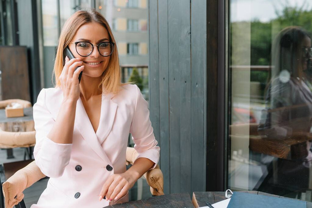 Smiling businesswoman dressed in formal wear having pleasant conversation on mobile phone with friend, happy attractive female speaking on cell telephone while resting in office interior after work - Foto, imagen
