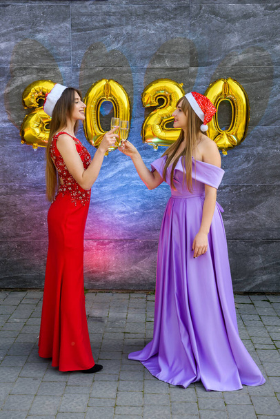 Gelukkige meisjes met champagne en gouden luchtballonnen in elegante avondjurken die nieuwjaar vieren - Foto, afbeelding