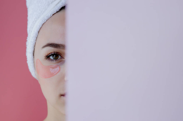 Portrait of Beauty Woman with Eye Patches on pink background. Woman Beauty Face with Mask under Eyes. Skin care, cosmetic product concept with copy space. - 写真・画像