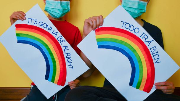 Irmãos usar uma máscara verde descartável com mensagem de esperança e arco-íris em folhas oblíquas de papel na frente deles
 - Foto, Imagem