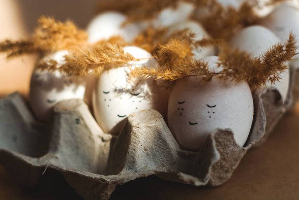 Χαρούμενα Πασχαλινά και λευκά αυγά στο δίσκο με τα χαριτωμένα πρόσωπα σε στεφάνια από αγκάθια. - Φωτογραφία, εικόνα