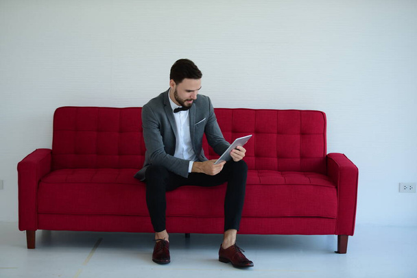 молодой человек в красном костюме сидит на диване с ноутбуком
 - Фото, изображение