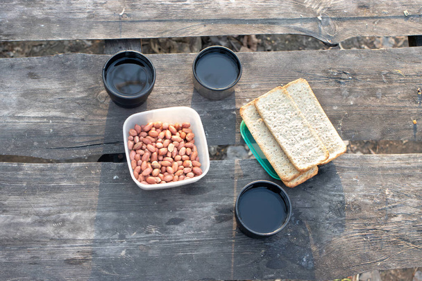 Picknick in der Natur: grüner heißer Tee aus der Thermoskanne, geröstete Erdnüsse, Brot. Mittagessen an der frischen Luft. - Foto, Bild