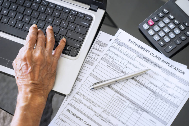 Retirement claim application form with senior man hand and laptop on the table - Φωτογραφία, εικόνα