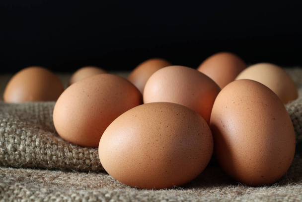 Tuoreet kananmunat säkissä mustalla taustalla, kotitekoisen luomuruoan konsepti
. - Valokuva, kuva