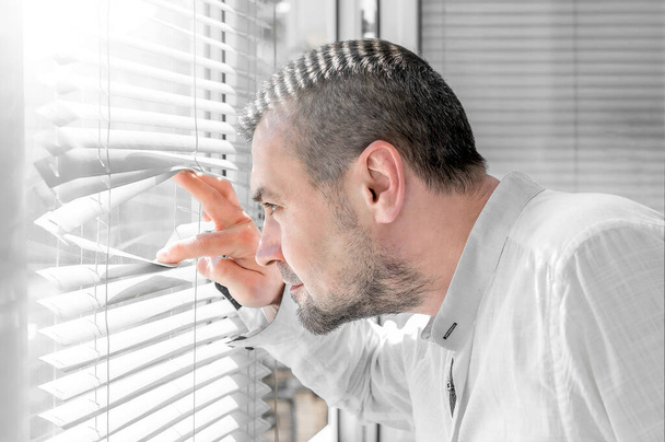 Hombre aislado mirando a través de persianas. Brote de Coronavirus. El hombre mira una calle soleada a través de las persianas de la ventana - Foto, imagen