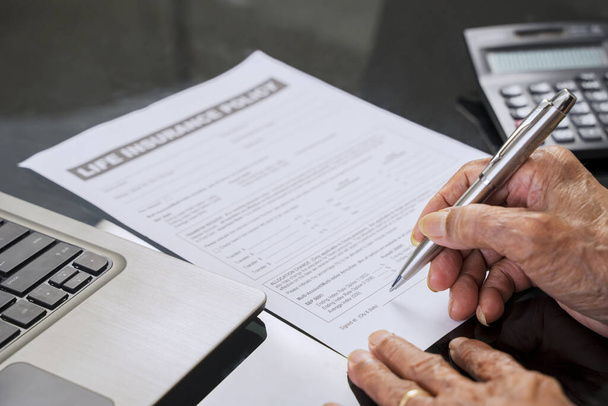 Senior man hand signing a life insurance claim form on the table at home - Φωτογραφία, εικόνα
