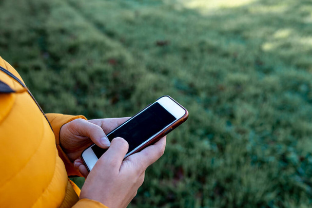 Gros plan des mains d'une jeune femme tapant sur son smartphone avec de l'herbe en arrière-plan
 - Photo, image