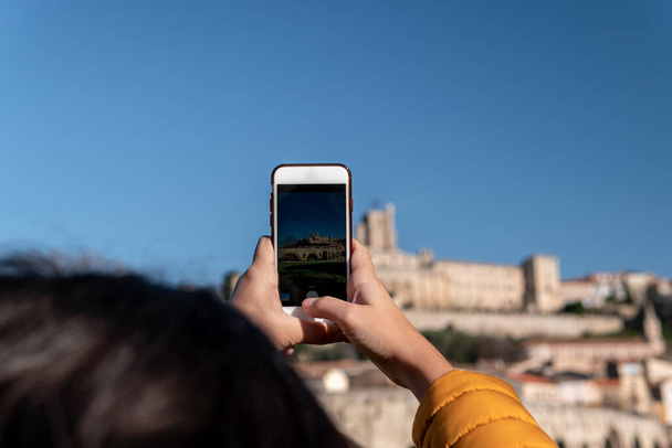 Nahaufnahme einer jungen Touristin, die mit ihrem Smartphone ein Foto von einer mittelalterlichen Burg macht. - Foto, Bild