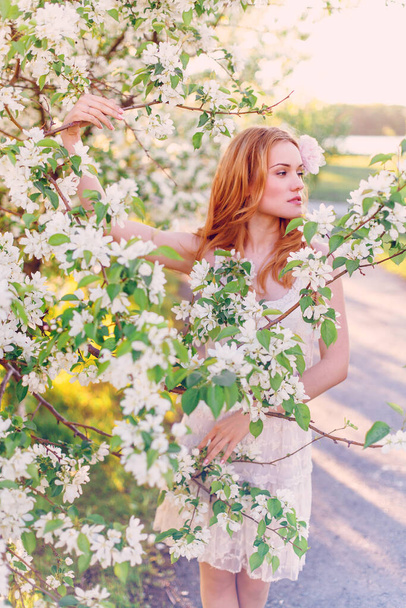 Model with red hair posing in a blooming apple tree. - Foto, Imagen