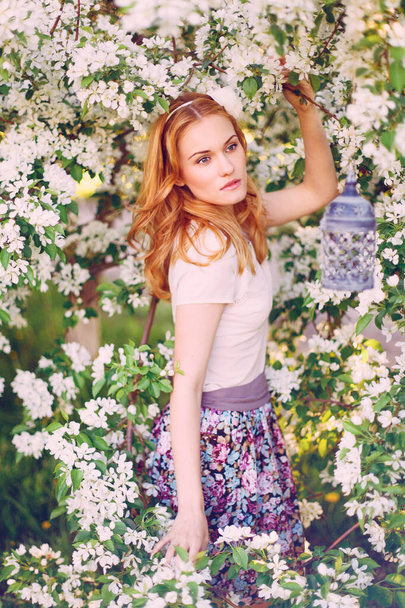 Model with red hair posing in a blooming apple tree. - Фото, зображення
