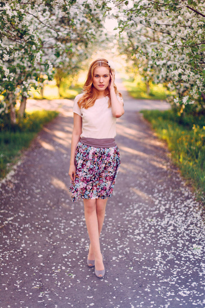 Model with red hair posing in a blooming apple tree. - Фото, зображення