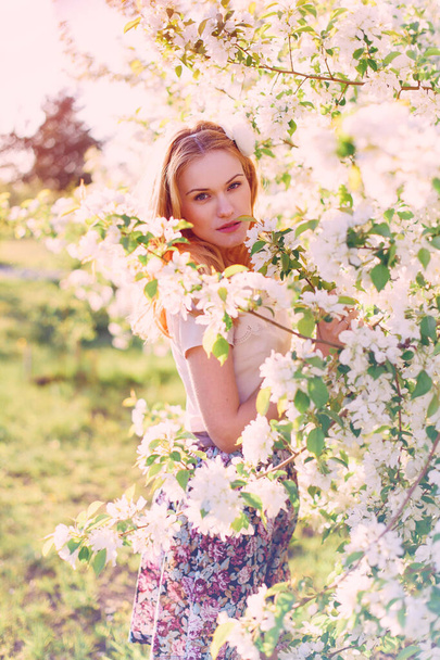 Model with red hair posing in a blooming apple tree. - Foto, immagini
