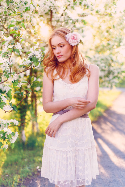 Model with red hair posing in a blooming apple tree. - Foto, immagini