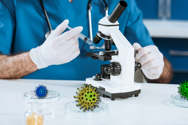 cropped view of scientist in latex gloves holding syringe near microscope, bacteria illustration - Valokuva, kuva