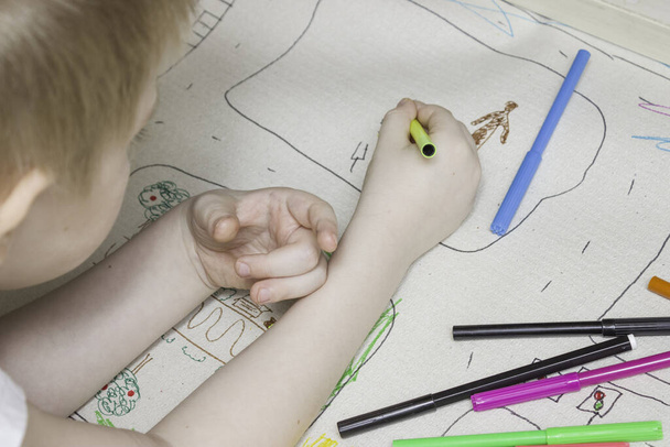 Der Junge zeichnet eine große Zeichnung, Seitenansicht. Markierungen sind in der Nähe. Konzept der Freizeit der Kinder, Zeichnen, Kinderkurse. Die Lektion im Kindergarten. - Foto, Bild