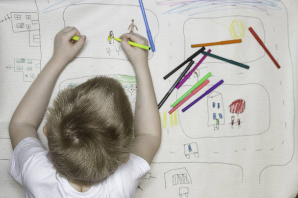 De jongen tekent een grote tekening, een uitzicht van achteren. Markers, de achterkant van het hoofd. Begrip vrijetijdsbesteding voor kinderen, tekenen, klassen voor kinderen. - Foto, afbeelding