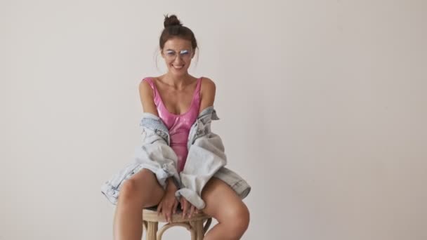 Cheerful stylish pretty brunette woman in swimsuit and eyeglasses having fun and looking at the camera near the wall - Filmagem, Vídeo