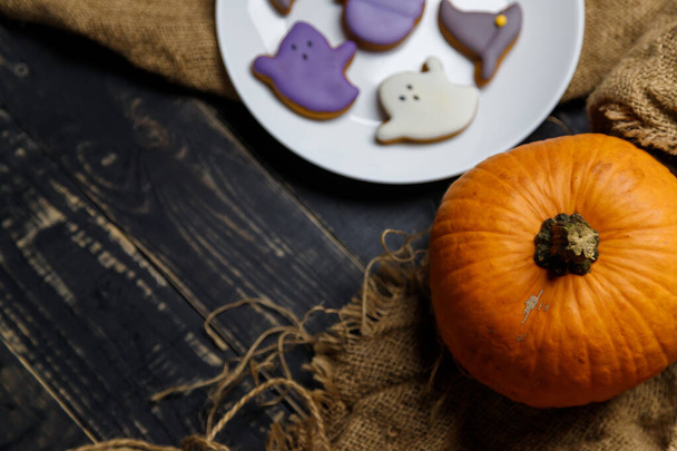 Pumpkin and Halloween cookies on white plate, sackcloth on black wooden background. Hallooween trick or treat concept. Copy space. - Photo, Image