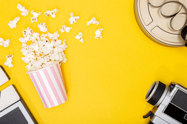 Popcorn-Eimer, Filmkamera, Dose und Klöppel auf gelbem Hintergrund. Film- oder TV-Hintergrund. Ansicht von oben Kopierraum - Foto, Bild