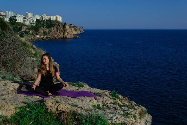 Belle jeune fille faisant de la méditation de yoga en position lotus à l'extérieur sur des rochers près de la mer bleue
  - Photo, image