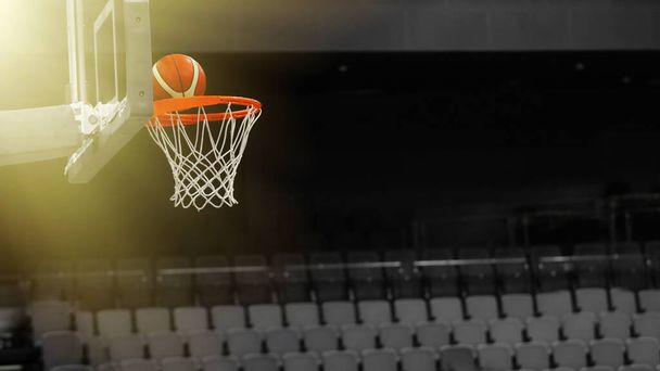 バスケットボールボールは、スポーツ複合体のスタンドの背景にあるバスケットボールのフープに飛び込みます - 写真・画像