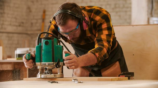 Timmerwerk industrie - man met beschermende bril en koptelefoon snijden van de patronen uit de houten plank - Foto, afbeelding