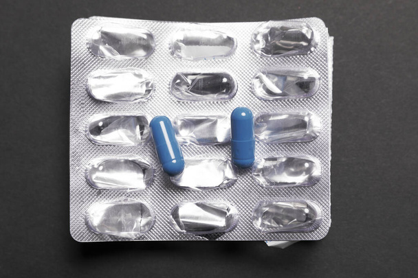 Blauwe pillen op lege verpakking op een zwarte achtergrond - Foto, afbeelding
