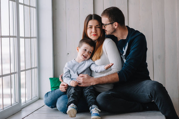 happy family of mother, father and child son playing and cuddling, at home on floor near a big window. Family concept - Foto, Imagen
