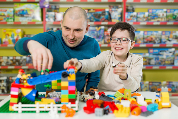 Father and son with happy faces create colorful constructions of toy bricks. Dad and kid build of plastic blocks. Family and childhood concept. - Photo, Image