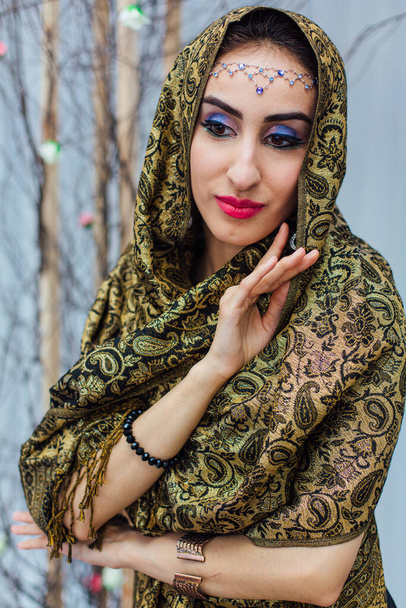 Close up portrait of a beautiful eastern woman with bright makeup and jewelry wearing headscarf. - Фото, зображення