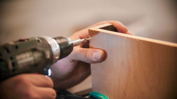 Indústria de carpintaria - trabalhador faz furos no pedaço de madeira compensada
 - Foto, Imagem