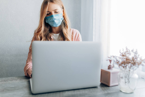 A young businesswoman works from home, sitting at a table with a laptop, wearing a protective mask. The concept of quarantine, coronavirus - Foto, Imagem
