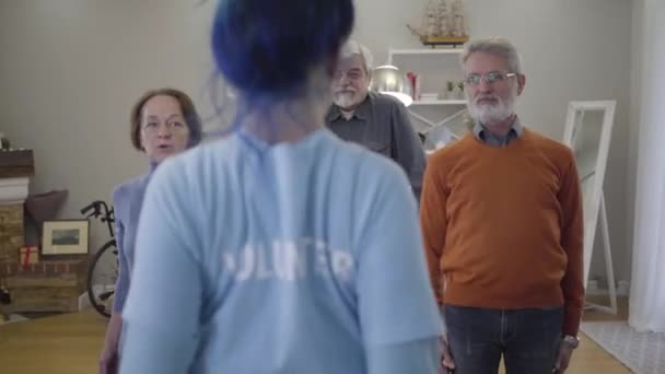 Three Caucasian retirees moving shoulders together with volunteer. Old men and woman exercising in the morning in nursing home. - Imágenes, Vídeo