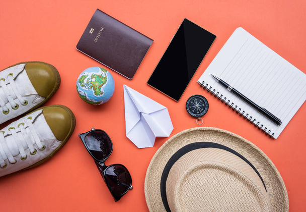 旅行アクセサリー、旅行休暇、スマートフォン、コンパス、帽子、靴、サングラス、パスポート、紙飛行機、オレンジ色の紙のノートブックの観光モックアップ - 写真・画像