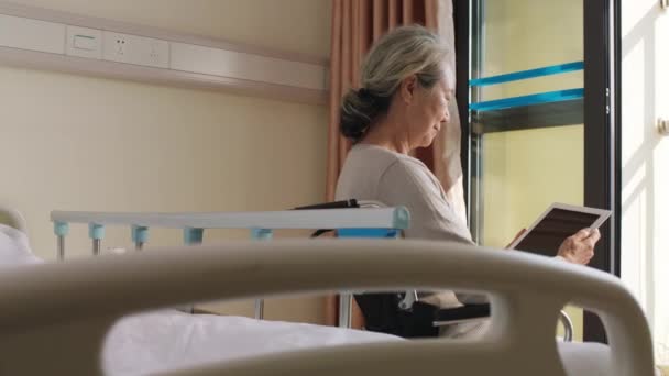 Ασιάτισσα ηλικιωμένη γυναίκα που κάθεται σε αναπηρικό καροτσάκι στο γηροκομείο χρησιμοποιώντας ψηφιακή ταμπλέτα - Πλάνα, βίντεο