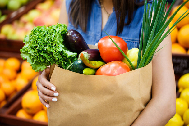 A close-up paper bag with vegetables and fruits in female hands  - Foto, immagini