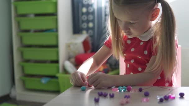 Ein kleines Mädchen fertigt ein Armband aus Perlen - Filmmaterial, Video