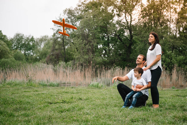 Father, mother and son playing with toy airplane in the park. friendly family. People having fun outdoors. Picture made on the background of the park and blue sky. concept of a happy family. - Foto, Imagen