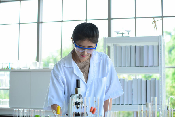 Junge Wissenschaftlerinnen experimentieren mit Wissenschaft im Labor.Asiatische Wissenschaftlerin mit Reagenzglas in einem Labor, Nahaufnahme einer Wissenschaftlerin, Junge Wissenschaftlerin, die durch ein Mikroskop in einem Labor forscht, Medizin für kovid19. - Foto, Bild