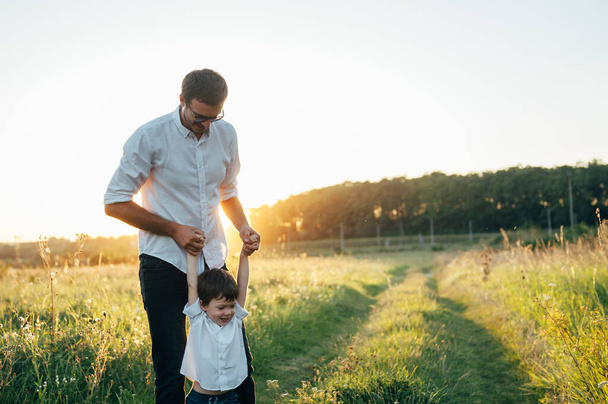 Handsome dad with his little cute son are having fun and playing on green grassy lawn. Happy family concept. Beauty nature scene with family outdoor lifestyle. family resting together. Fathers day - 写真・画像