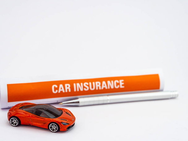 Een speelgoedauto met gedecentraliseerd verzekeringspapier achter en balpen op  - Foto, afbeelding