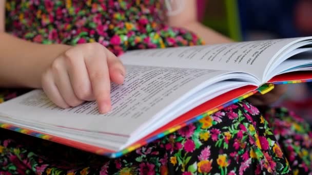 カラフルなドレスの少女は本を読んでいる。子供は読むことを学ぶ. - 映像、動画