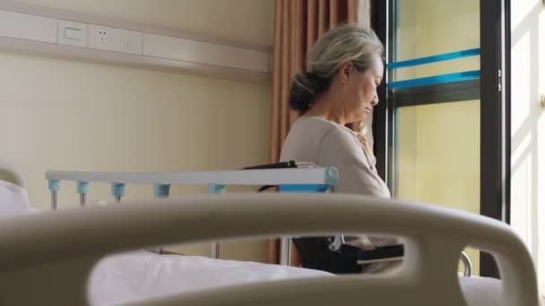 Ασιάτισσα γριά που κάθεται μόνη της σε αναπηρική καρέκλα στο δωμάτιό της στο γηροκομείο - Πλάνα, βίντεο