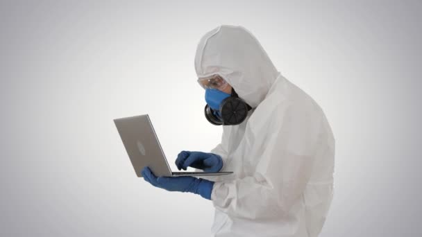 Doctor in protective suit working on laptop and having good results on gradient background. - Кадры, видео