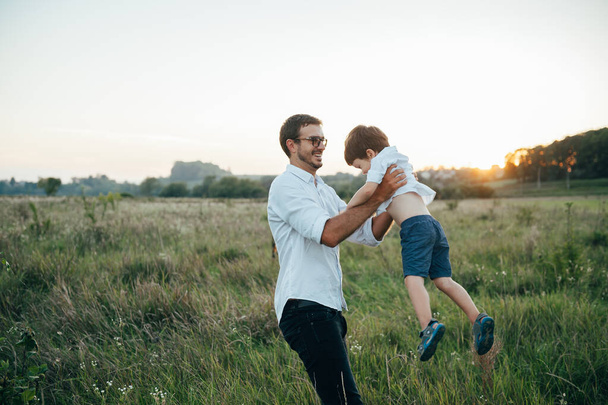 Handsome dad with his little cute son are having fun and playing on green grassy lawn. Happy family concept. Beauty nature scene with family outdoor lifestyle. family resting together. Fathers day - Foto, afbeelding